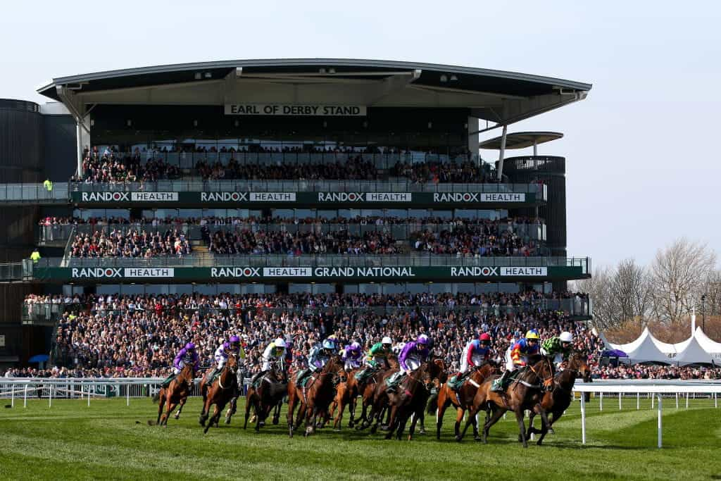 Huge crowds pack an Aintree grandstand as the runners gallop by.