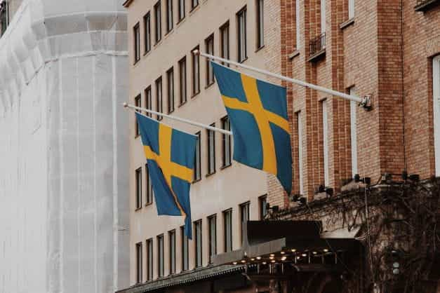 Two Swedish flags hanging at an angle from the front of a building.