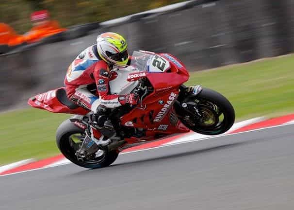 A person in a helmet and full professional riding gear riding a motorcycle during a professional race on a closed track.