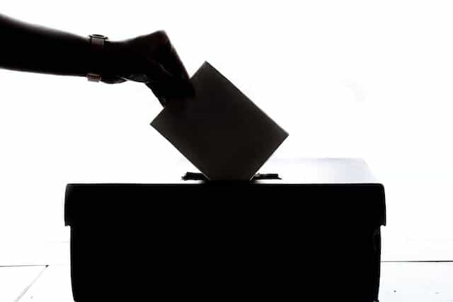 A silhouette of a hand dropping a ballot into a ballot box.