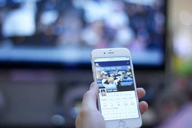 A person holding up a smartphone in front of a television screen.