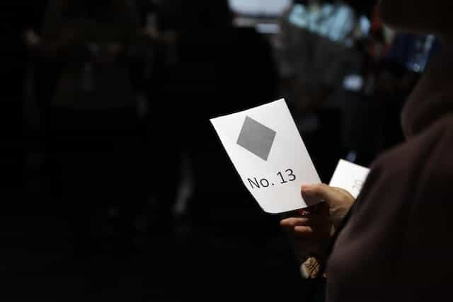 Someone holds a piece of paper with the text, No. 13 and a grey diamond shape printed on it.