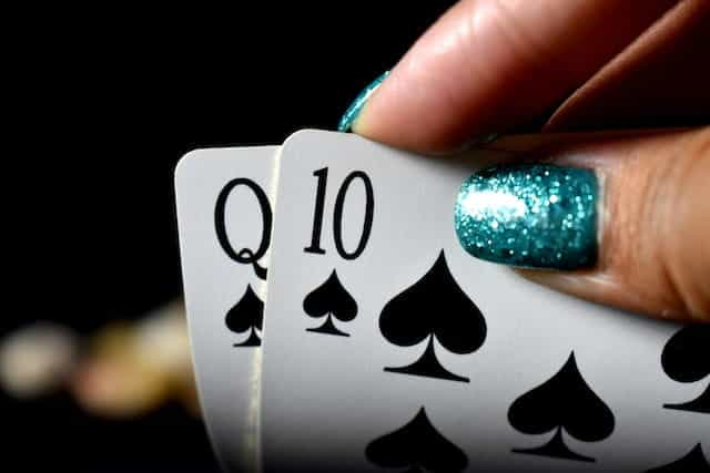 A hand with painted nails holding playing cards.