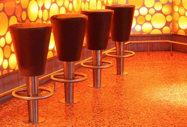 Four fixed barstools at a bar with a lit-up pattern design running along the side of the bar.