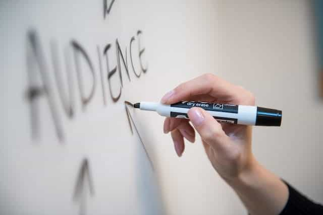 Close up of female hand writing the word audience on whiteboard.