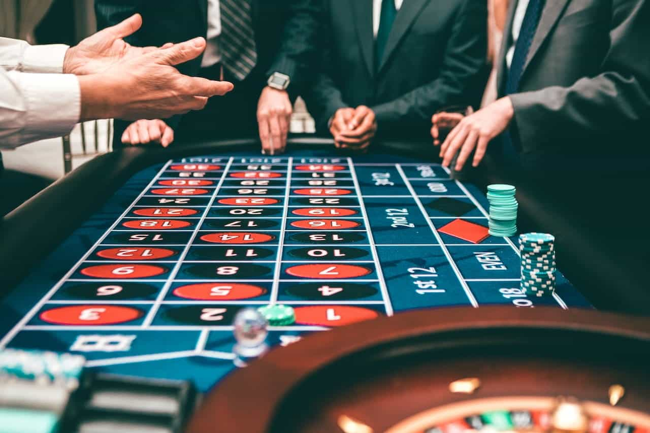 Men in suits gamble at a roulette wheel in a casino. 