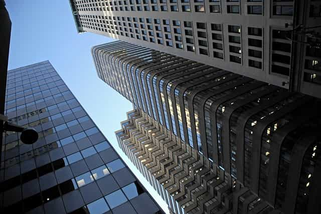 A low-down, ground level shot looking upwards at several tall skyscrapers in the middle of a city’s downtown district.