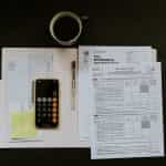 A worktop from above with various tax paperwork, a calculator and a cup of coffee.