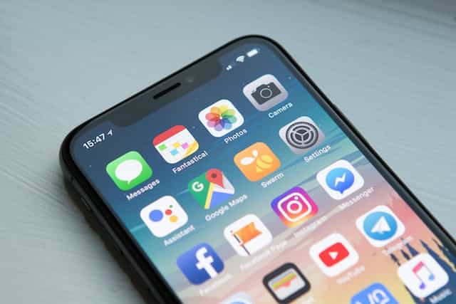 The main screen of an Apple iPhone lying flat on a table, showcasing several basic apps.