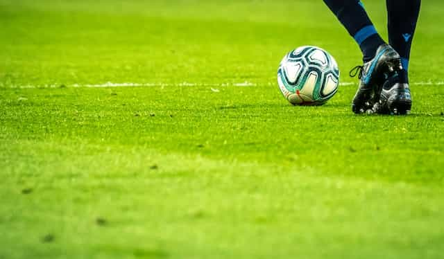 A ball and a pair of soccer player’s legs and shoes on grass.