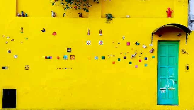 A highly decorated bright yellow wall and blue-green door in Salta, Argentina.